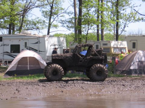 1999 Chevrolet Avalanche - Off-road vehicle covered in mud at a campsite with RVs and tents in the background.