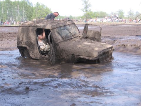 1999 Chevrolet Avalanche - A heavily mud-caked Jeep Wrangler is stuck deep in a muddy mire, with two individuals attempting to free it.