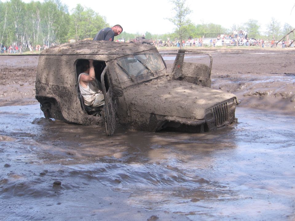 Mud-covered Jeep Wrangler stuck in mud with people inside and on top