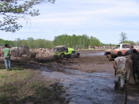 1999 Chevrolet Avalanche - Multiple off-road vehicles navigate a muddy track during an event, with spectators watching from the sidelines.