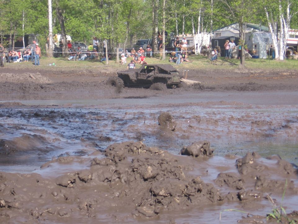 Mud-covered off-road truck driving through a muddy track with spectators in the background