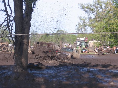 1999 Chevrolet Avalanche - Multiple vehicles are deeply stuck in mud during an event, with spectators and a tractor nearby.