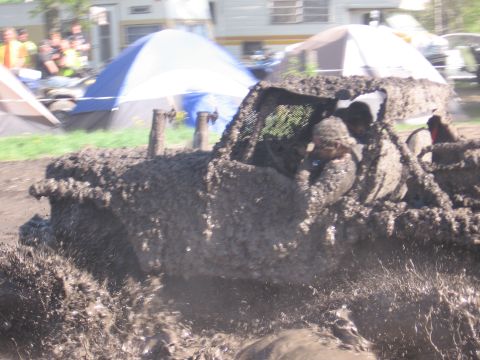 1999 Chevrolet Avalanche - Off-road vehicle covered in mud, with people inside, driving through a muddy area.