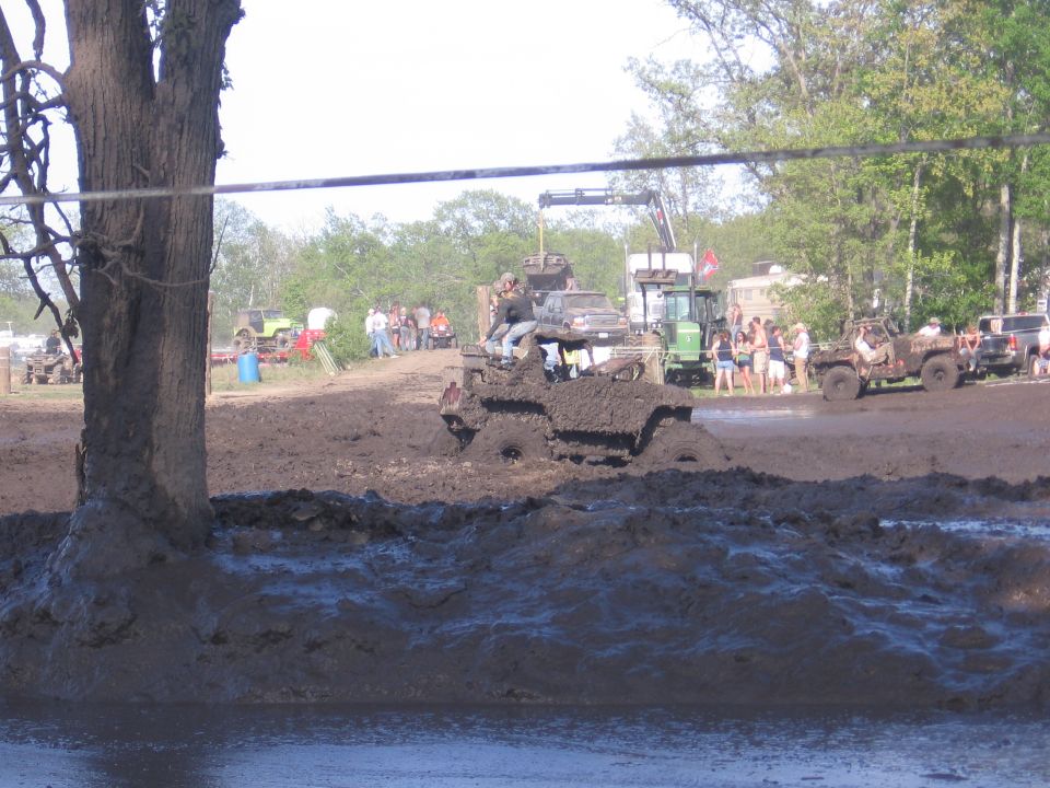 Mud-covered open-body 4x4 buggy bogged in a mud pit with spectators watching