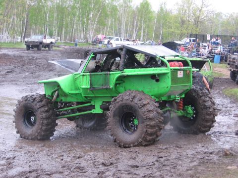 1999 Chevrolet Avalanche - A heavily modified off-road buggy navigates a muddy course with spectators watching from bleachers.