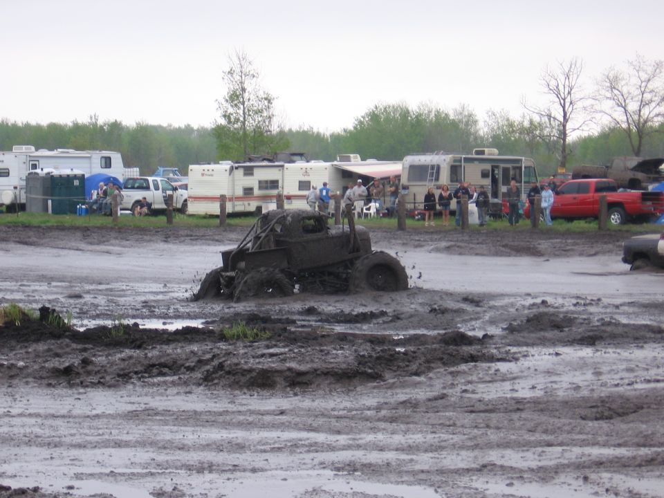 Mud-covered off-road truck stuck axle-deep in a mud bog with spectators and RVs behind