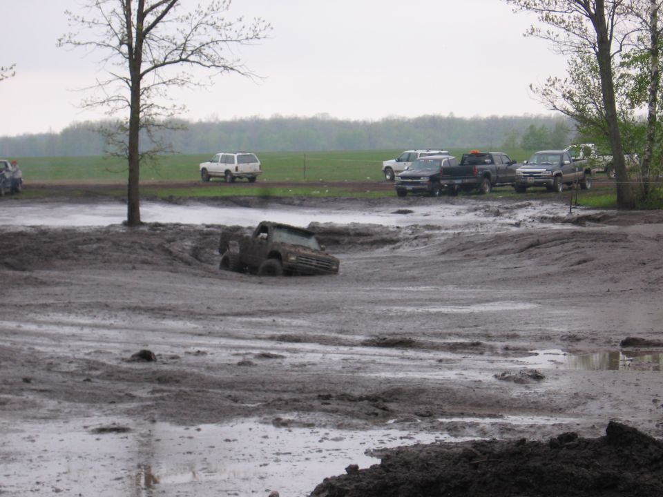 Muddy pickup stuck in a mud pit with trucks parked in the background