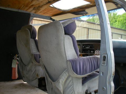 1978 Ford E250 - The interior of a van shows two rows of seats and a damaged ceiling with a skylight.
