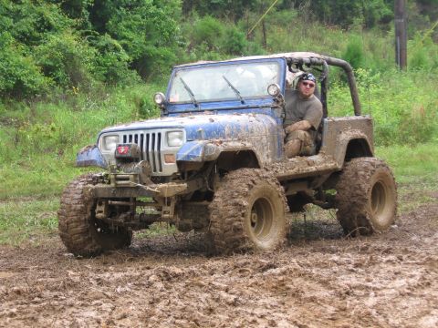 1967 Ford Mustang - A blue Jeep Wrangler navigates a muddy terrain with its driver visible.