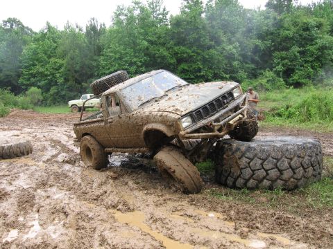 1967 Ford Mustang - An off-road pickup truck navigates a muddy obstacle course, with another vehicle visible in the background.