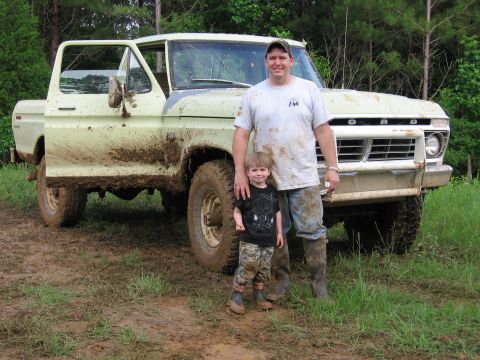 1967 Ford Mustang - A father and son pose in front of a dirty 1975 Ford F-Series truck, its driver's door open.