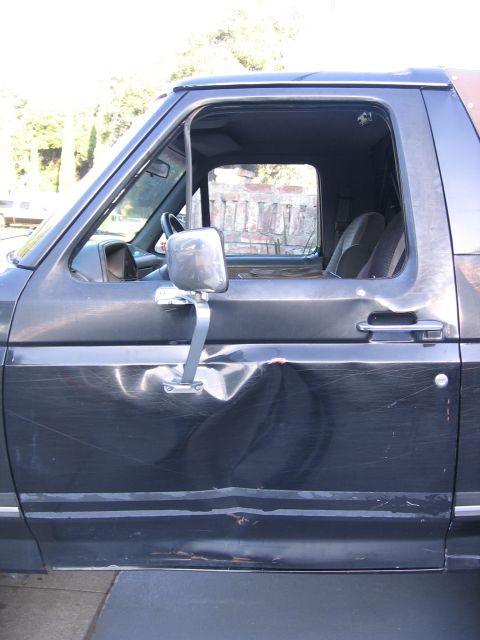 1989 Ford Bronco - The driver's side door of a 1989 Ford Bronco shows extensive damage and wear.