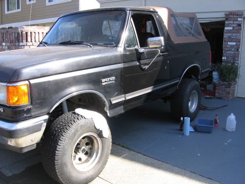 1989 Ford Bronco - Black 1989 Ford Bronco with lifted suspension and tan soft top parked in a driveway.