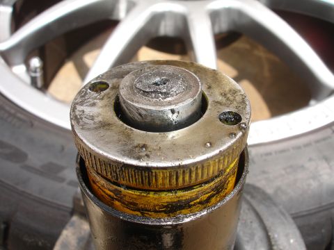 1993 Ford Taurus - Worn strut mount showing grease and metal fatigue, with a car wheel visible.