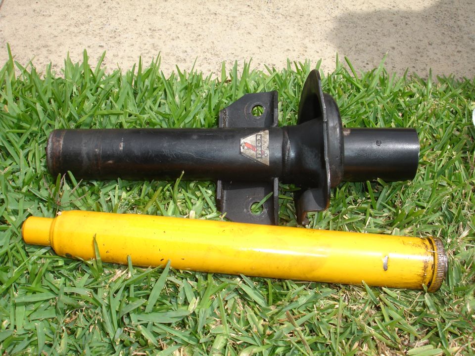 Black car strut with a red and white label, and a yellow spring assembly, lying on grass