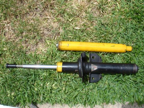 1993 Ford Taurus - Two car struts, one yellow and one black, are laid out on a grassy surface. The black strut is extended, showing its internal components.