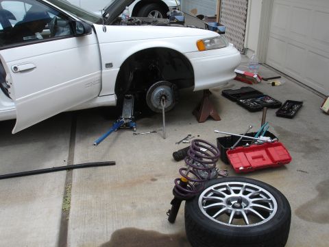 1993 Ford Taurus - A car is undergoing maintenance with its front wheel off and various tools laid out on the ground.