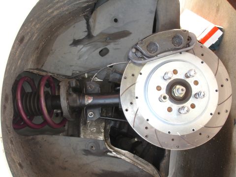 1993 Ford Taurus - Close-up view of a car's front suspension and braking system, showing a coilover shock and a drilled brake rotor.