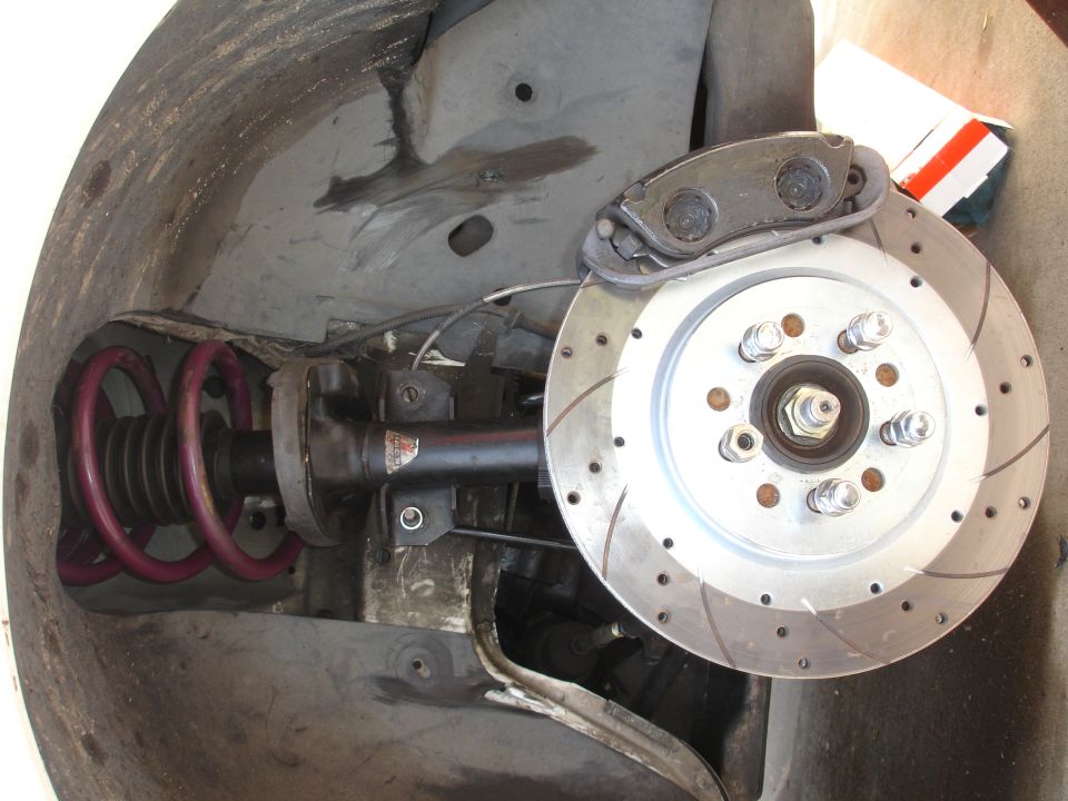 Car's front suspension with a purple coilover spring and a drilled brake rotor with a silver caliper