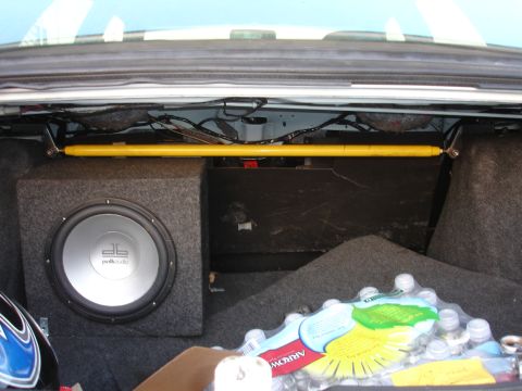 1993 Ford Taurus - The interior of a car trunk shows a subwoofer, a yellow strut bar, and a pack of bottled water.
