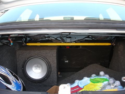 1993 Ford Taurus - The trunk of a car contains a subwoofer, a yellow strut bar, and bottled water.
