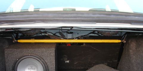 1993 Ford Taurus - The trunk of a car shows a yellow strut bar installed above a subwoofer enclosure and wiring.