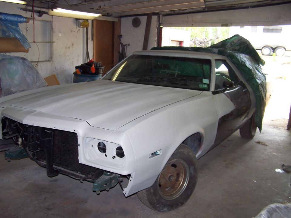 Ford Ranchero with white-primered front clip and green rear body, front end stripped, in garage