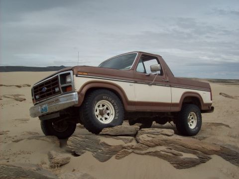 1985 Ford Bronco - This Ford Bronco is navigating rocky terrain under a cloudy sky.
