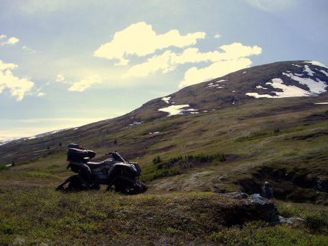 2000 Ford E350 - An all-terrain vehicle sits parked on a grassy slope below a mountain with patches of snow.