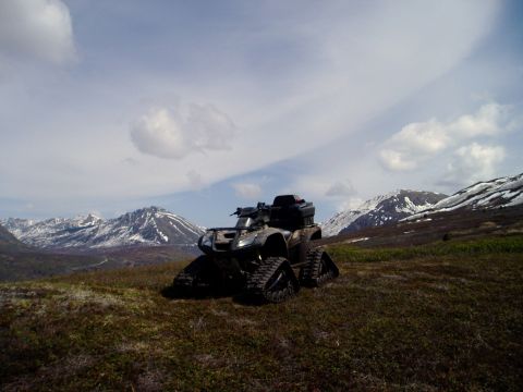 2000 Ford E350 - An all-terrain vehicle equipped with tracks sits on a hill overlooking a mountain range under a cloudy sky.