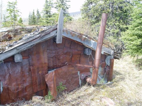 2000 Ford E350 - An old, weathered shack sits in a wooded area, its corrugated metal walls showing significant rust.