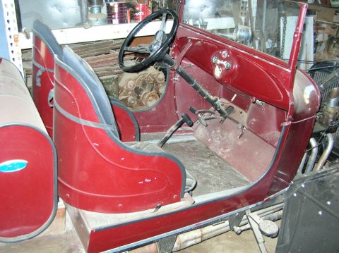 1930 Ford Model A - The interior of a vintage car shows red bucket seats and a dashboard with a steering wheel and gauges.