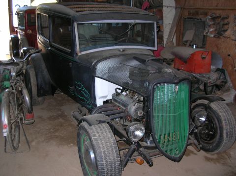 1931 Ford Model A - A modified hot rod with a distinctive green grille sits in a garage next to another vehicle.