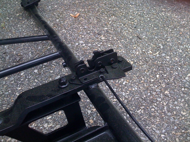 close-up of black metal frame parts and a latch assembly on asphalt
