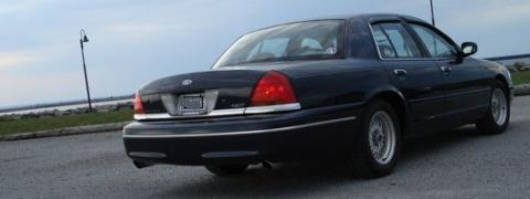 2000 Ford Crown Victoria - A black 2000 Ford Crown Victoria sedan is parked on asphalt with a body of water in the background.