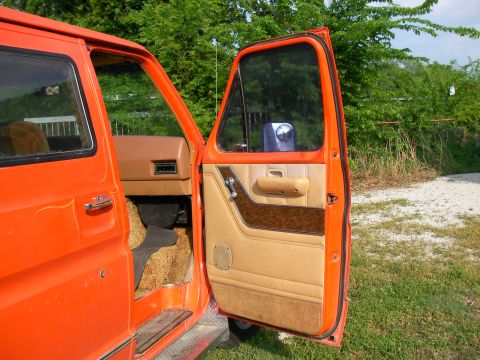 1978 Ford E150 - Interior view of an orange van with the driver's door ajar, revealing the tan and brown door panel.