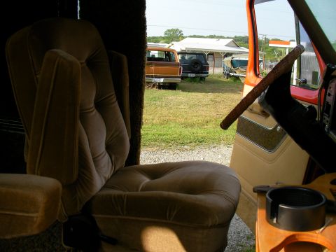 1978 Ford E150 - View from inside a 1978 Ford E150 van, showing the plush captain's chair and a glimpse of other vehicles parked outside.