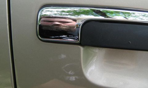 2000 Mercury Grand Marquis - A close-up of a vehicle's door handle shows a distorted reflection of a person's face.