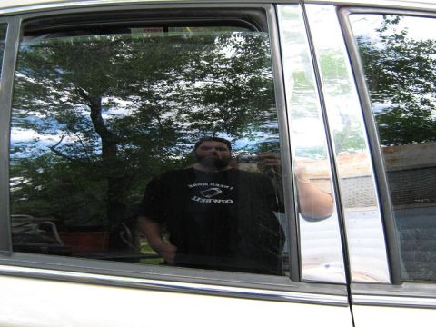 2000 Mercury Grand Marquis - The side window of a 2000 Mercury Grand Marquis reflects a man and the surrounding trees.
