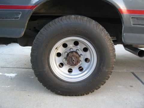 1986 Ford Bronco - A close-up view of a vehicle's wheel and tire, with a red stripe accent on the body panel.