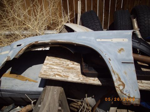 1982 Toyota 4Runner - A detached car fender sits in front of a wooden fence, with tires and debris in the background.