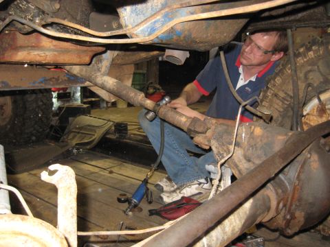 1978 Ford Bronco - Mechanic performs maintenance on the underside of a vehicle, focusing on the drivetrain components.