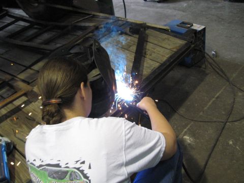 1978 Ford Bronco - A person is welding a metal frame on a wooden trailer in a workshop.