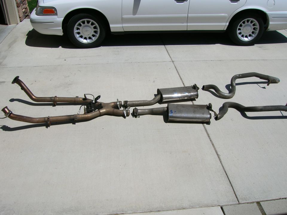Complete dual exhaust system laid out on a driveway behind a sedan