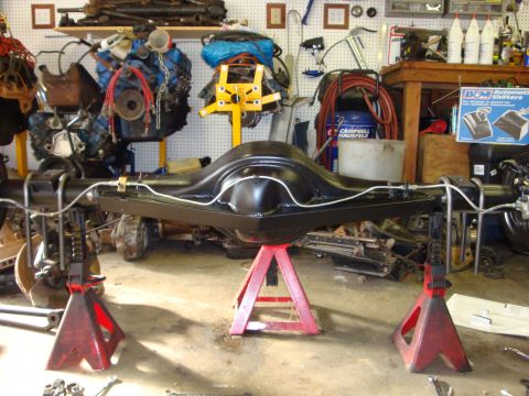 1989 Ford Bronco - A freshly painted rear axle assembly is supported by red jack stands in a cluttered garage workshop.