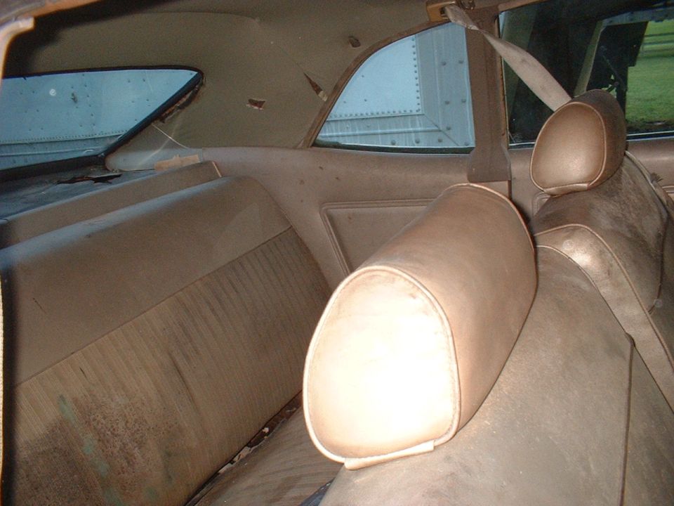 Back seat and headrests of a car interior. Seats are tan and worn