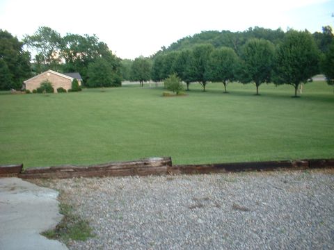 1971 Ford Torino - A wide shot captures a rural landscape a brick house, manicured lawn, and a line of trees under a hazy sky.