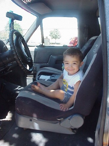 1989 Ford Bronco - Young child sitting and smiling in a child safety seat strapped into the cab of a truck.