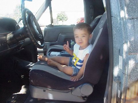 1989 Ford Bronco - Young child sits in the driver's seat of a vehicle, looking at the camera.