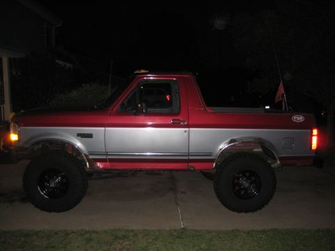 1995 Ford Bronco - Side view of a lifted 1995 Ford Bronco with two-tone red and silver paint.